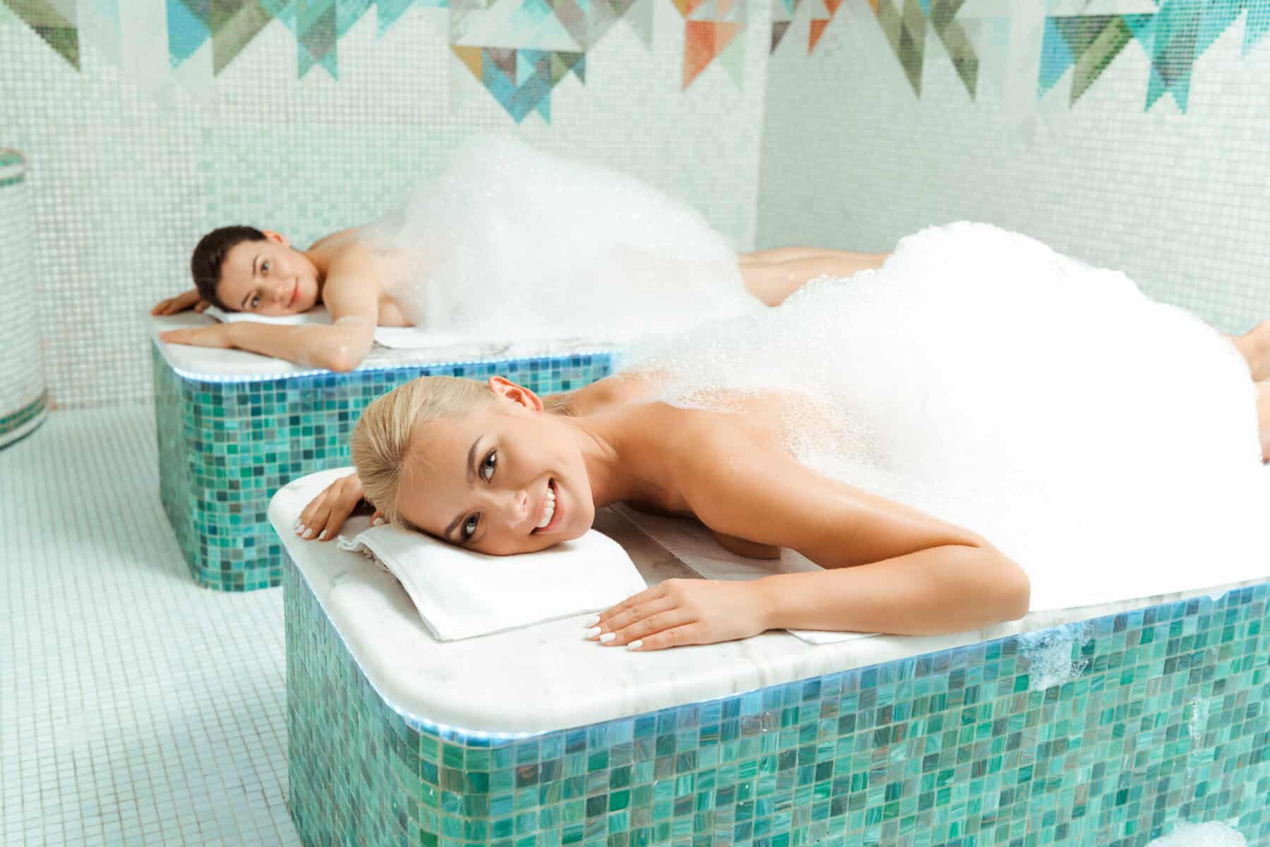 attractive and smiling friends lying with foam in turkish bath